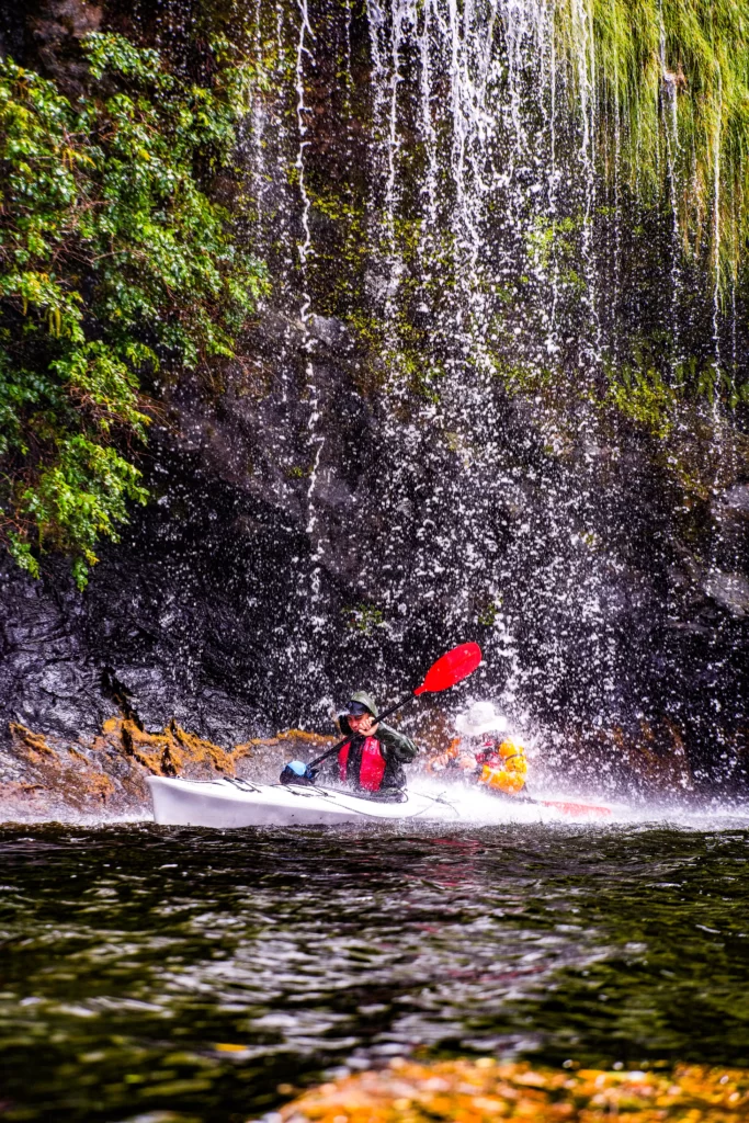 Kayaker paddles under waterfall in Fiordland